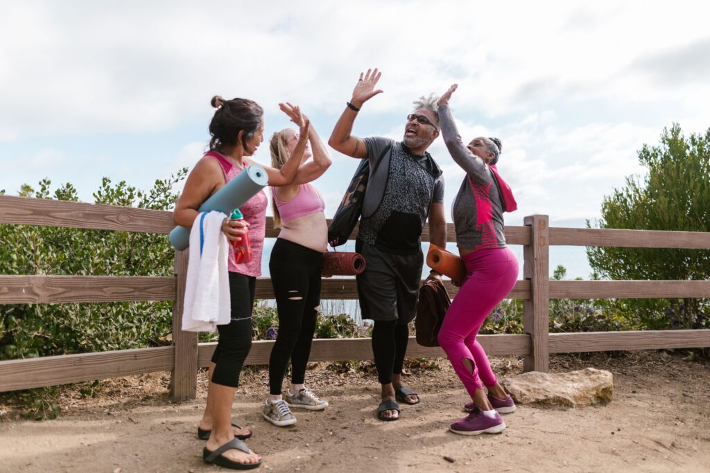 Senior group in activewear high-fiving outdoors, embracing fitness and joy.